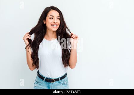 Giovane donna che posa e sorride, lisciando i capelli su sfondo bianco Foto Stock