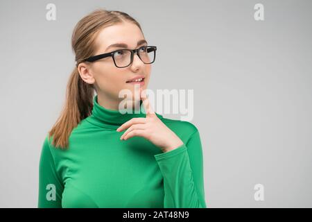 Giovane ragazza in piedi occhiali è pensierosa in studio e cercando. - Immagine Foto Stock