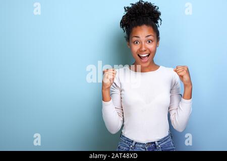 La donna eccitata si presenta con pugni trincerati nel gesto del vincitore in studio. Gesto concettuale - immagine Foto Stock