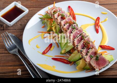 Cucina giapponese. Tataki con tonno. Pesce fritto con semi di sesamo e salsa di soia, wasabi, lime. Su un cuscino di verdure. Avocado, strisce di peperoncino Foto Stock