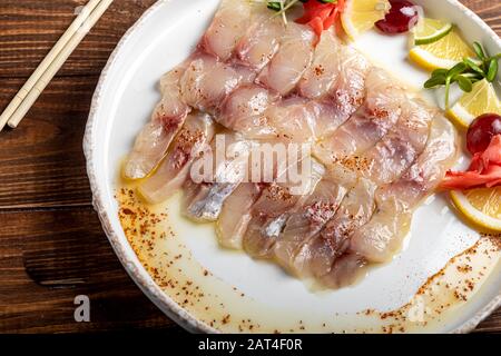 dorado leggermente salato con girasole in olio di tartufo. Accanto a fettine di limone, lime, uva, zenzero sottaceto. Sul lato della piastra sono presenti bacchette. Acceso Foto Stock