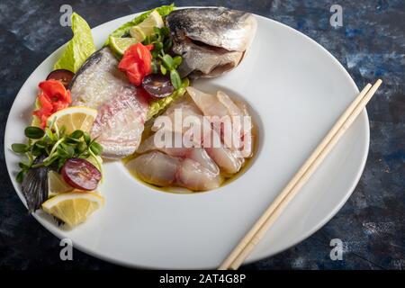 dorado leggermente salato con girasole in olio di tartufo. Accanto a fettine di limone, lime, uva, zenzero sottaceto. Sul lato della piastra sono presenti bacchette. Acceso Foto Stock