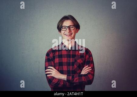 Allegro ragazzo hippster teenage, indossando casual camicia rossa e occhiali, mantiene le mani piegate guardando gioioso alla fotocamera isolato su sfondo grigio parete. Foto Stock