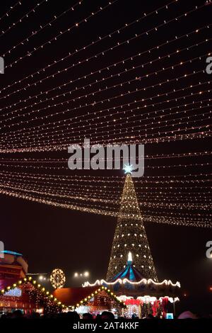 Un albero di Natale con una grande stella sopra di esso e alcune piccole case decorate nello spirito di Natale Foto Stock