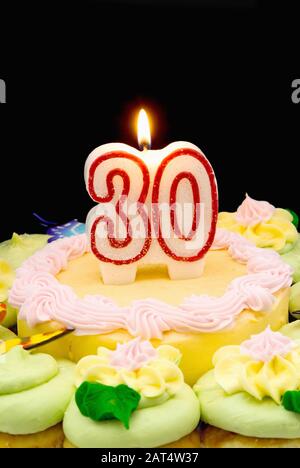 Torta di compleanno e cupcakes con un numero 30 cera che brucia candela sulla parte superiore. Lo sfondo nero fornisce spazio di copia. Foto Stock