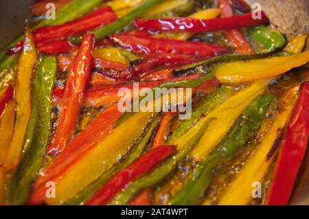 Primo piano di una teglia in cui i peperoni tagliati a strisce vengono fritti, sono peperoni rossi, verdi e gialli in abbondante olio caldo Foto Stock