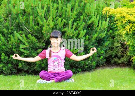 Ragazza dai capelli neri sorride e pratica yoga nel parco. Ragazza seduta in posizione lotus, medita, sport estivi, Dnipro, Ucraina, 16.05.2018. Foto Stock