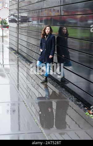 Donna che riflette quattro volte in un contemporaneo edificio in metallo nero e sotto la pioggia Foto Stock