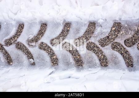 Tracce di un pneumatico del trattore su asfalto nevoso su una strada in inverno. Foto Stock