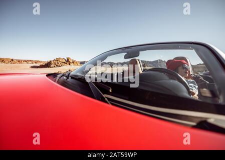 Giovane donna che viaggia in auto convertibile nella pittoresca valle del deserto, seduto al posto di guida. Vista frontale attraverso il parabrezza Foto Stock