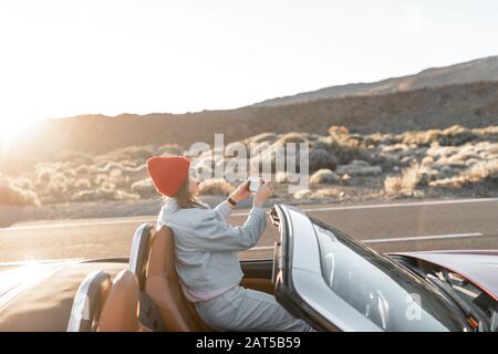 Ritratto di stile di vita di una giovane donna che si gode viaggio su strada nella valle del deserto, seduto sulla macchina convertibile sulla strada Foto Stock