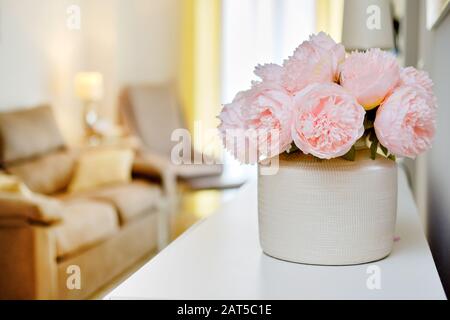 Bella colore rosa peonies fiori in vaso bianco all'interno di luce calda soggiorno, selettiva primo piano Focus sul bouquet, nessuna gente Foto Stock