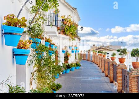 Scenario idilliaco vuoto pittoresca strada di piccolo villaggio bianco-lavato di Mijas. Percorso decorato con piante pendenti in fioriere blu luminoso Spagna Foto Stock