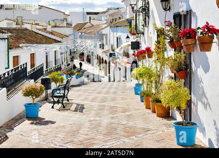 Scena idilliaca pittoresca strada piccolo bianco-lavato villaggio di Mijas. Percorso modo decorato con appesi su case pareti piante in fioriere luminose, fam Foto Stock