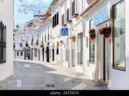 Mijas strada bianca lavata, piccolo villaggio famoso in Spagna. Affascinanti stradine vuote con decorazioni di Capodanno, su case muri appesi vasi di fiori Foto Stock