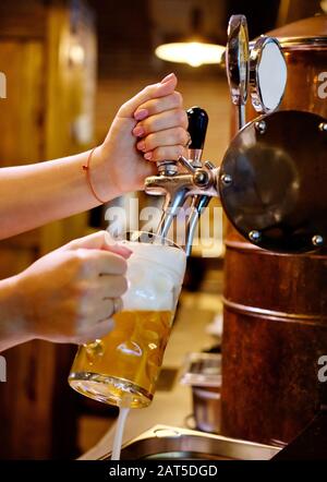 Immagine verticale primo piano vista donne barman mani versare la birra in tazza, bevande alcoliche servite da un rubinetto Foto Stock