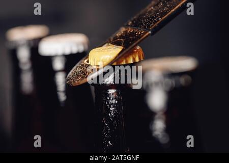 Bottiglie di birra ghiacciate in vetro con tappo apriscatole su sfondo scuro Foto Stock