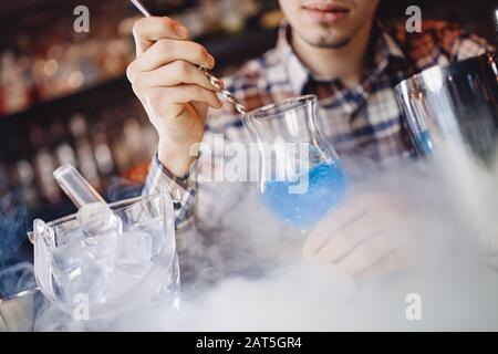 Il barman mescola un cocktail show blu con un colorato banco bar con alcolici e fumo Foto Stock