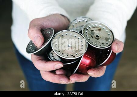 Una donna che tiene una manciata di cialde o capsule di caffè usati in alluminio da una macchina da caffè Nespresso. I baccelli vengono conservati per essere riciclati Foto Stock