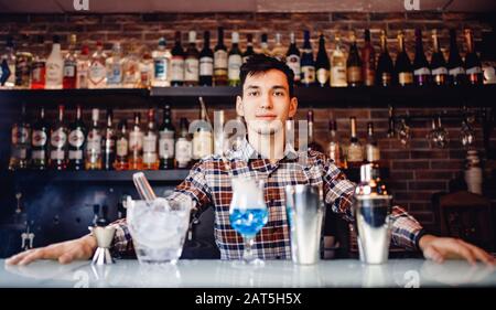 Il barman mescola un cocktail show blu con un colorato banco bar con alcolici e fumo Foto Stock