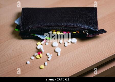 un portafoglio femminile con carte bancarie che si stacchino si trova sul tavolo. Un gran numero di pillole può essere visto nel portafoglio Foto Stock