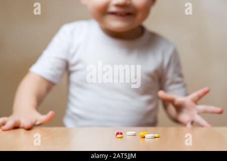pillole sul tavolo e sorridente bambino in defocus. Il bambino sta per prendere pillole dal tavolo Foto Stock