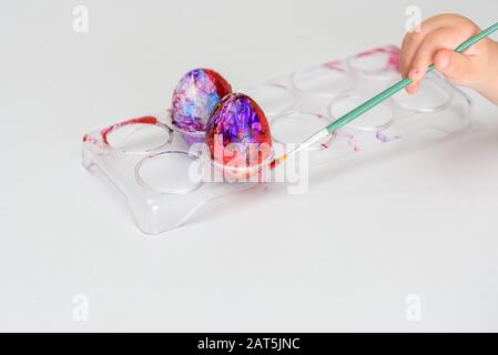 Bambino mani dipinte di uova di Pasqua, vernici e spazzole sul tavolo bianco. Preparazione per la Pasqua. Kid mani disegnare con colori. Foto Stock