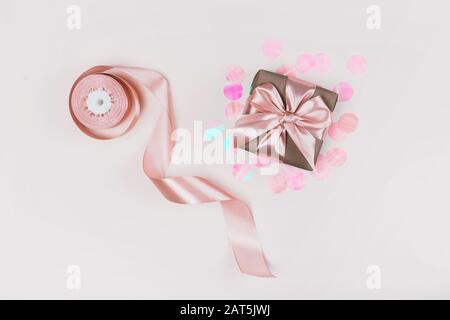 Confezione regalo confezionata in carta artigianale con nastro rosa perfetto su sfondo rustico rosa pallido con confetti olografici. Foto Stock