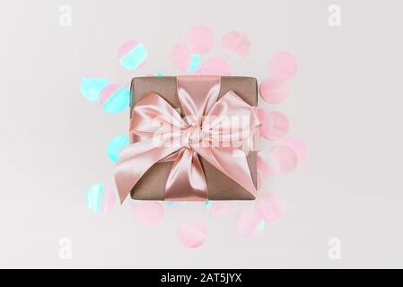 Confezione regalo confezionata in carta artigianale con nastro rosa perfetto su sfondo rustico rosa pallido con confetti olografici. Foto Stock