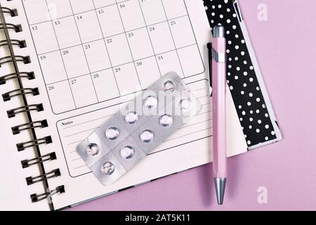 Concetto per il controllo delle nascite con calendario mensile, penna e confezione blister di piccole pillole su sfondo rosa Foto Stock