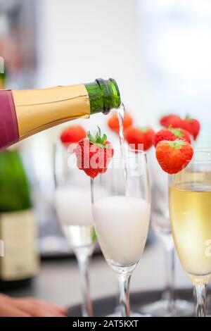 Spumante o champagne e fragola su uno sfondo sfocato che viene versato dalla bottiglia durante una sorta di festa o celebrazione come un matrimonio, un giorno di borthday o un anno nuovo Foto Stock