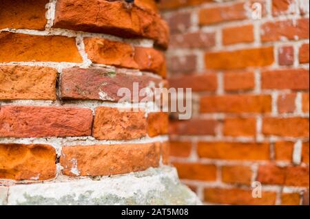 Parte di un vecchio palo di mattoni a fuoco e un muro di mattoni sullo sfondo in defocus. Parte di un edificio abbandonato Foto Stock