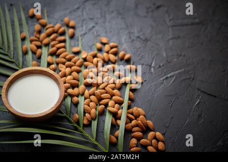 Semi di mandorle con ciotola di latte fresco naturale posto su sfondo di pietra nera Foto Stock