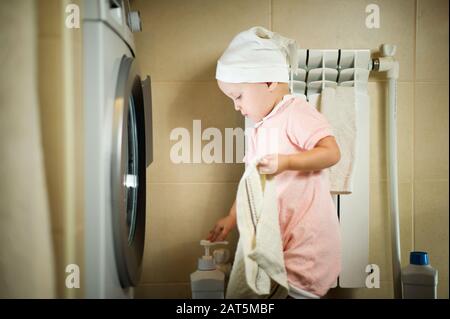 La bambina si trova di fronte ad una lavatrice con un asciugamano in mano. Primo piano Foto Stock