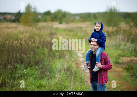 il bambino siede sulle spalle del padre. Camminare nel villaggio. Spazio di copia Foto Stock