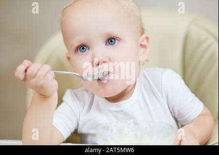 la bambina mangia porridge e guarda in modo sognante davanti a sé stessa. Spazio di copia Foto Stock