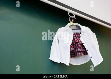 Vestiti della scuola di un bambino piccolo appesi su un appendiabiti vicino alla lavagna, vista dal basso Foto Stock