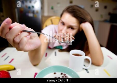 la ragazza guarda purtroppo il cucchiaio con scaglie di cioccolato che sta tenendo davanti a sé stessa. Piano generale, grandangolo, messa a fuoco selettiva Foto Stock