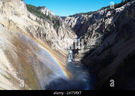 La nebbia che arriva dalla forza delle cascate inferiori di Yellowstone crea un arcobaleno di fronte al fiume durante il viaggio lungo il canyon. Foto Stock