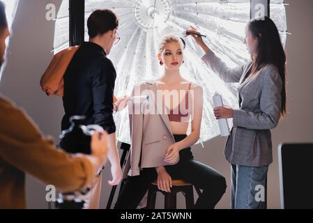 messa a fuoco selettiva dello stilista usando rullo di pelucchi e hairstylist che fa l'acconciatura al modello elegante sul backstage Foto Stock