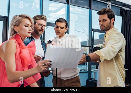 attraente modello e bel direttore artistico guardando collage di foto con fotografo e assistente Foto Stock