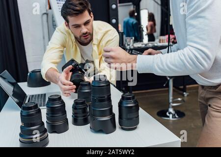 vista ritagliata del direttore artistico vicino al fotografo e alle lenti fotografiche Foto Stock