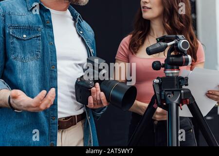 vista ritagliata del direttore creativo in piedi con il fotografo vicino al treppiede Foto Stock