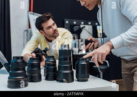 vista ritagliata del regista artistico che punta con il dito sull'obiettivo della fotocamera vicino al fotografo Foto Stock