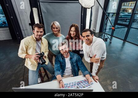 vista dall'alto di un buon direttore creativo e di assistenti che guardano la fotocamera in uno studio fotografico Foto Stock