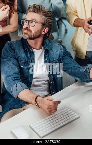 vista ritagliata degli assistenti che si trovano vicino al direttore artistico in occhiali Foto Stock