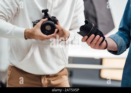 vista ritagliata del fotografo che tiene la macchina fotografica digitale vicino al direttore artistico con l'obiettivo della macchina fotografica Foto Stock