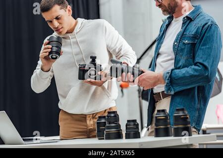 vista ritagliata del direttore artistico con lente fotografica vicino al fotografo Foto Stock