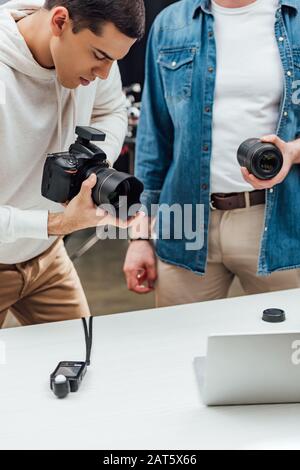 vista ritagliata del direttore artistico che tiene l'obiettivo vicino a un bel fotografo Foto Stock