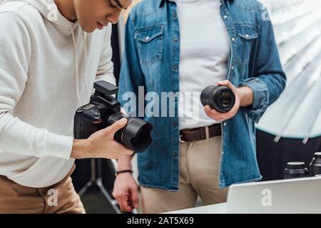 vista ritagliata del direttore artistico che tiene l'obiettivo vicino al fotografo Foto Stock